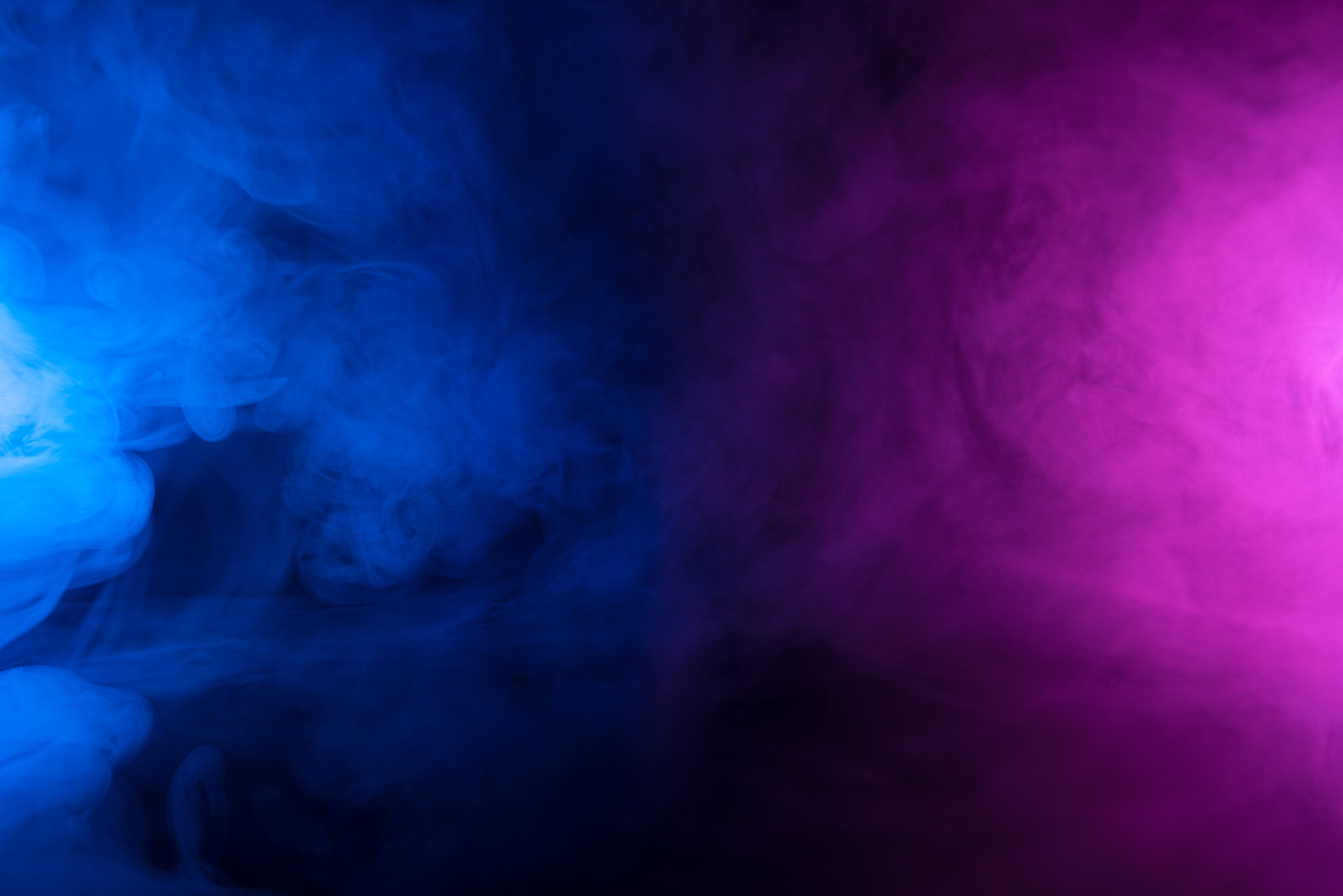 Clouds of colorful smoke in blue and purple neon light swirling on black table